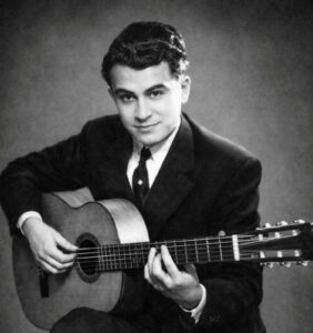Retrato de estudio vintage en blanco y negro de un joven Niño Ricardo. Viste traje oscuro y corbata, sosteniendo su guitarra flamenca en posición de toque. Es la imagen icónica del maestro que revolucionó el toque de acompañamiento y solista.